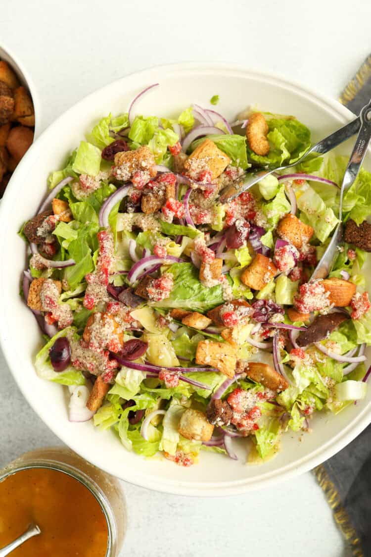 A large white serving bowl of Italian house salad with a jar of dressing next to it.