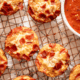 Pepperoni pizza muffins on a baking rack with a bowl of marina sauce.