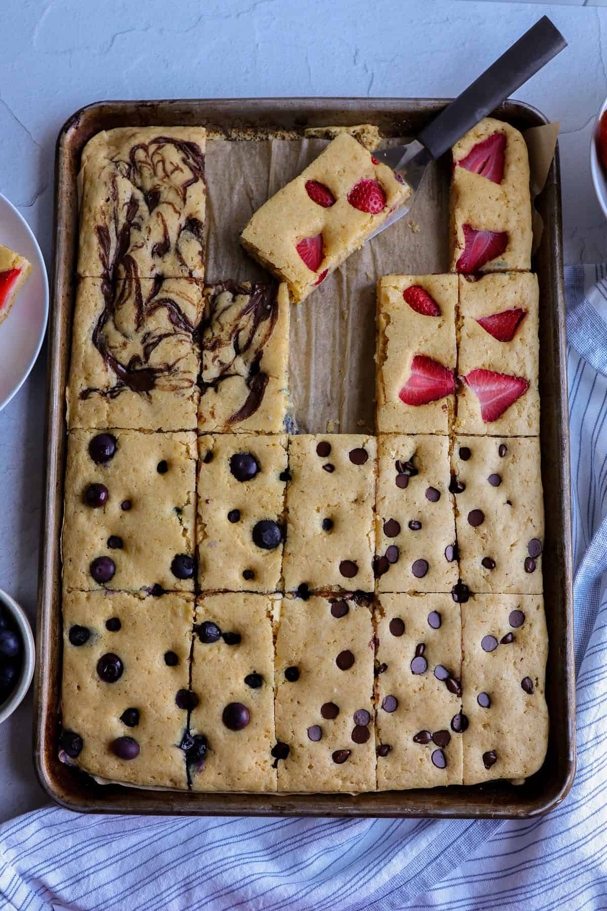 A baking pan of sheet pancakes with blueberries, strawberries, and chocolate chips mixed in separate areas of the pan.