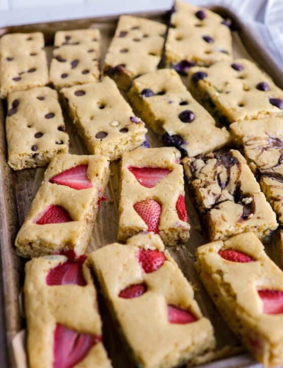 Slices of blueberry, chocolate chip, and strawberry sheet pancakes lined up on a baking sheet.