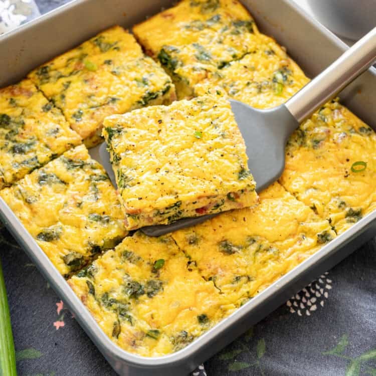 A slice of bacon spinach crustless quiche being served from a square baking dish.