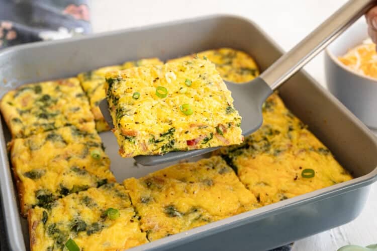 The middle serving of spinach bacon crustless quiche lifted out of the dish on a spatula.