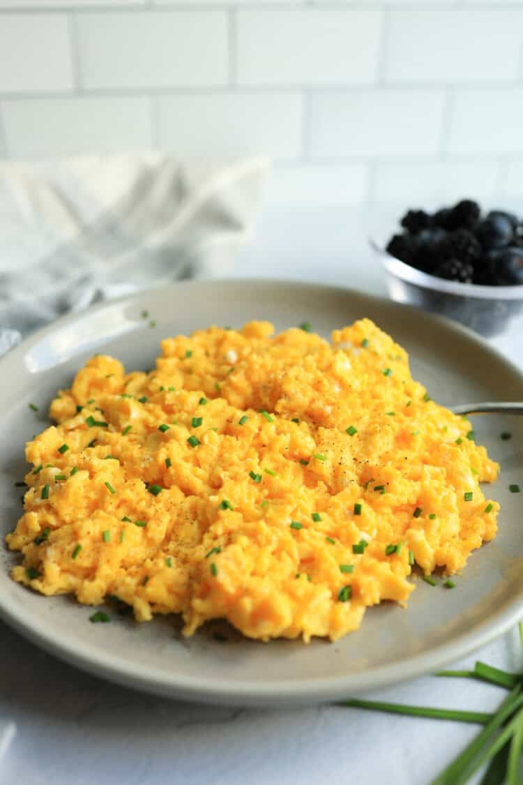 Scrambled eggs with cheese mixed in and chives on top served on a platter.