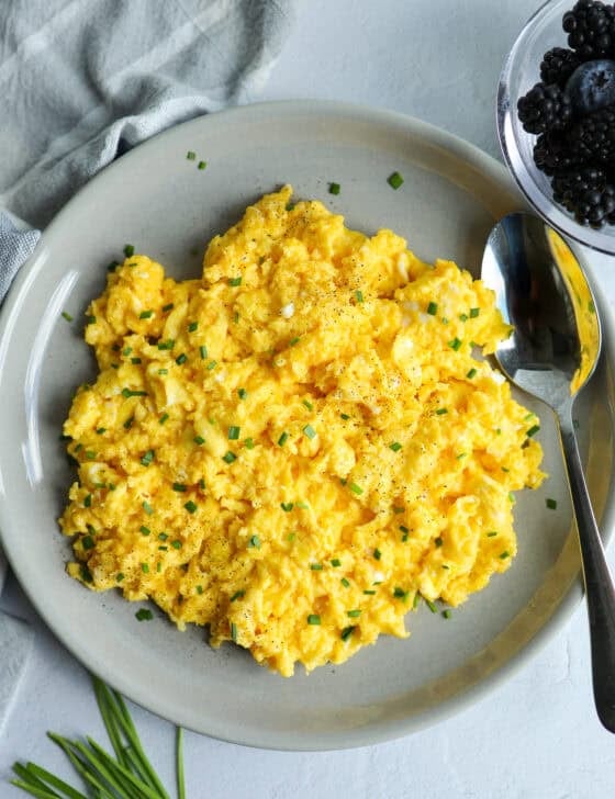 A platter of cheesy scrambled eggs and a bowl of fruit on a counter top.