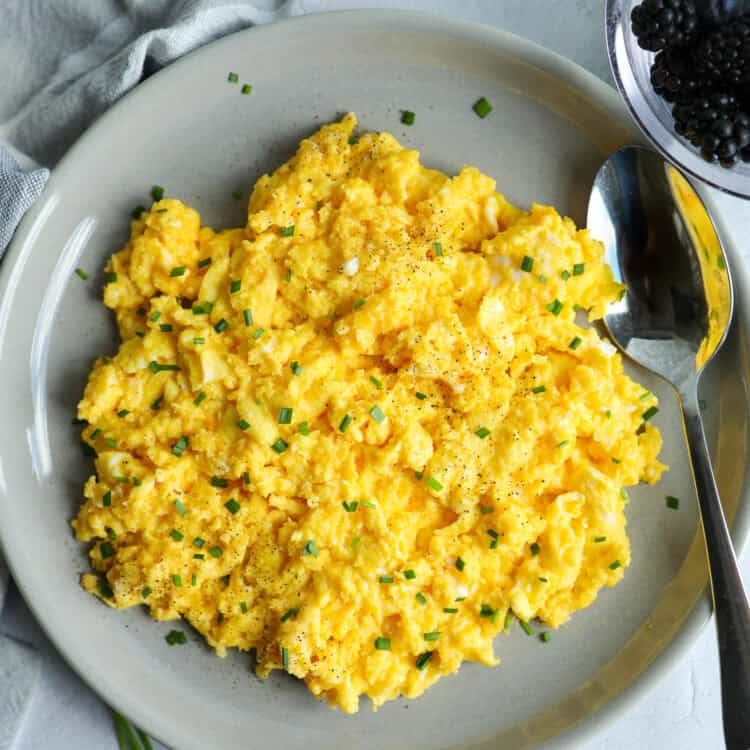 A platter of cheesy scrambled eggs and a bowl of fruit on a counter top.