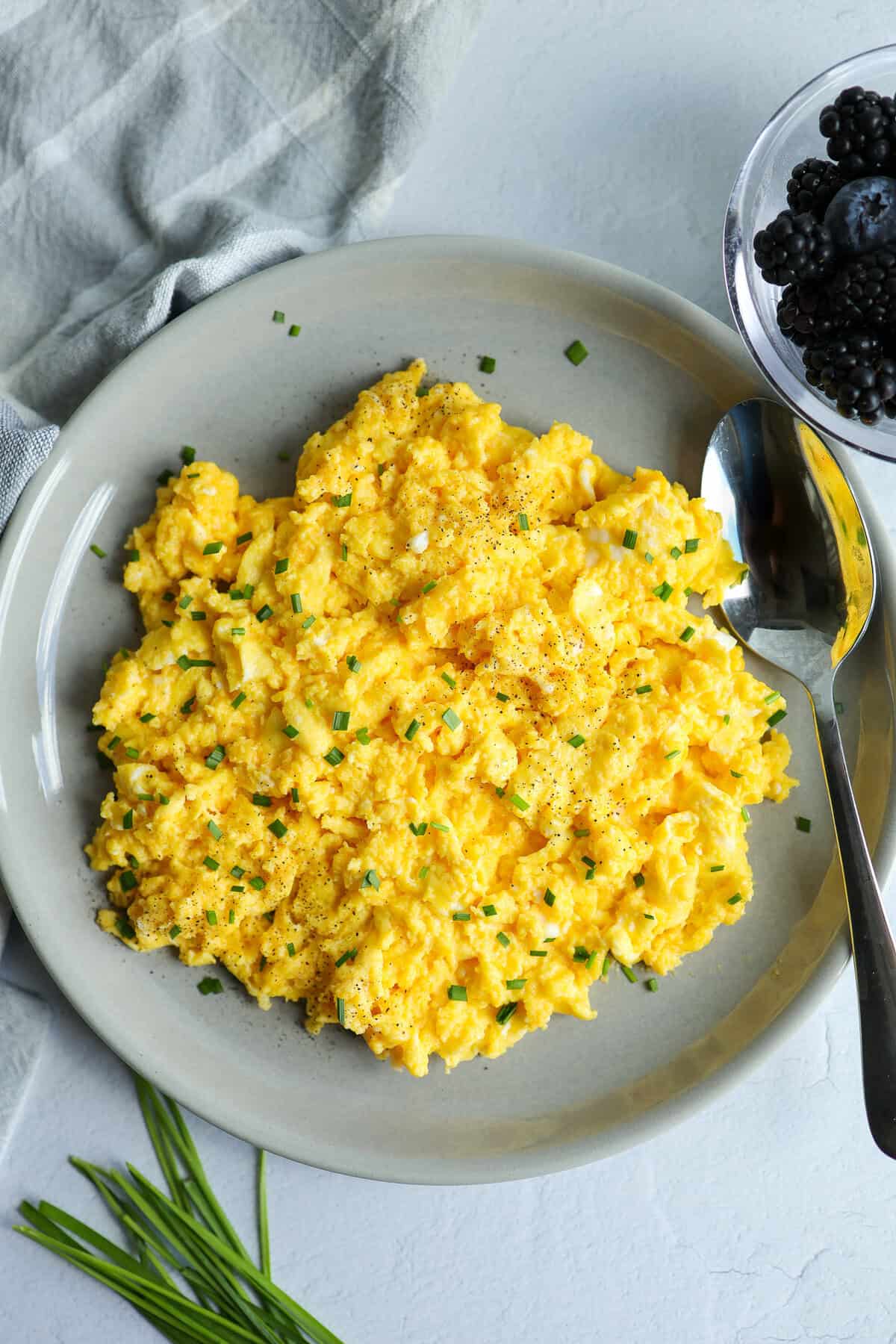 A platter of cheesy scrambled eggs and a bowl of fruit on a counter top.