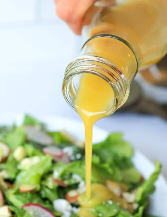 Honey Mustard Dressing poured out of a glass container onto a salad.