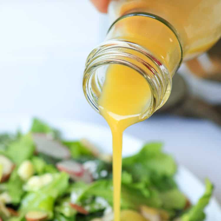 Honey Mustard Dressing poured out of a glass container onto a salad.