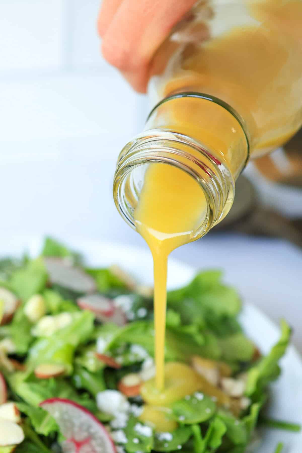 Honey Mustard Dressing poured out of a glass container onto a salad.