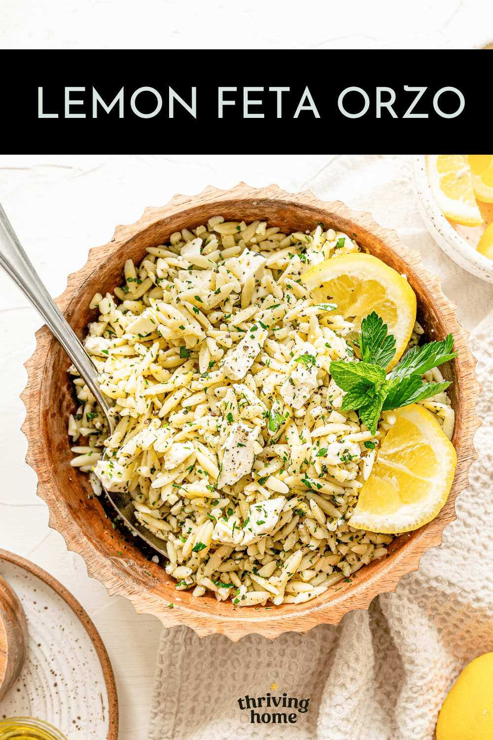 Lemon feta orzo in a wooden bowl served with fresh basil and lemon wedges.