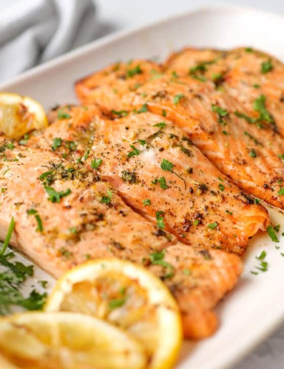 Salmon fillets with grilled lemon slices served with fresh chopped parsley on top.