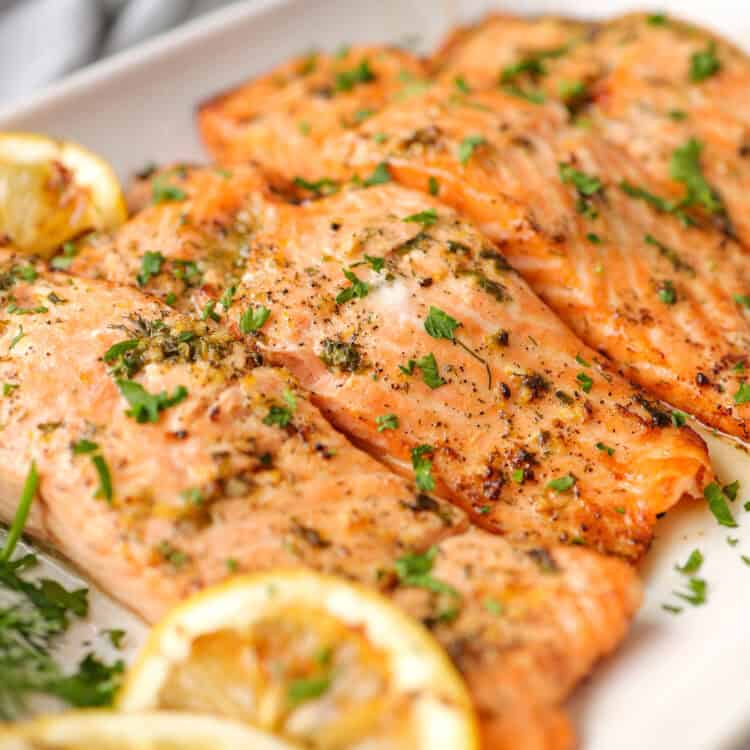 Salmon fillets with grilled lemon slices served with fresh chopped parsley on top.
