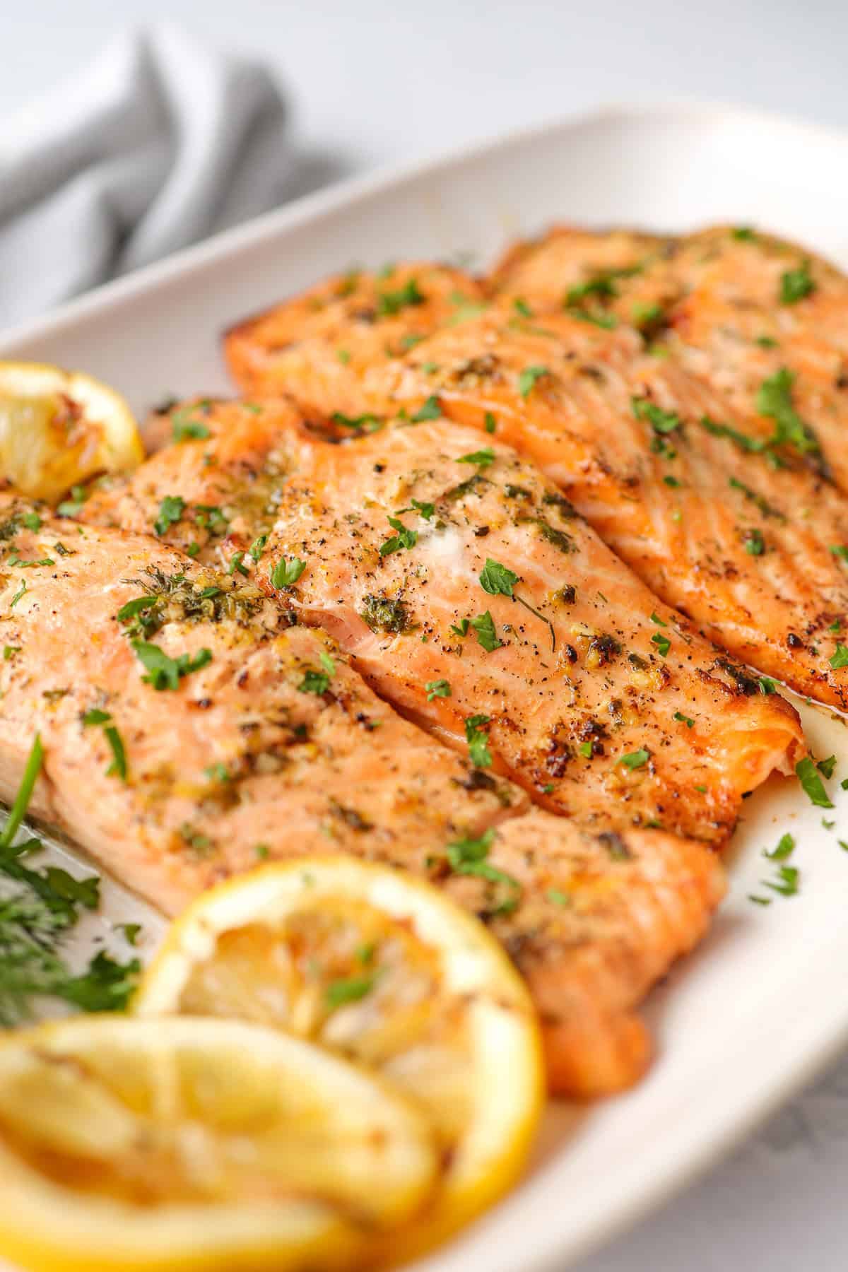 Salmon fillets with grilled lemon slices served with fresh chopped parsley on top.