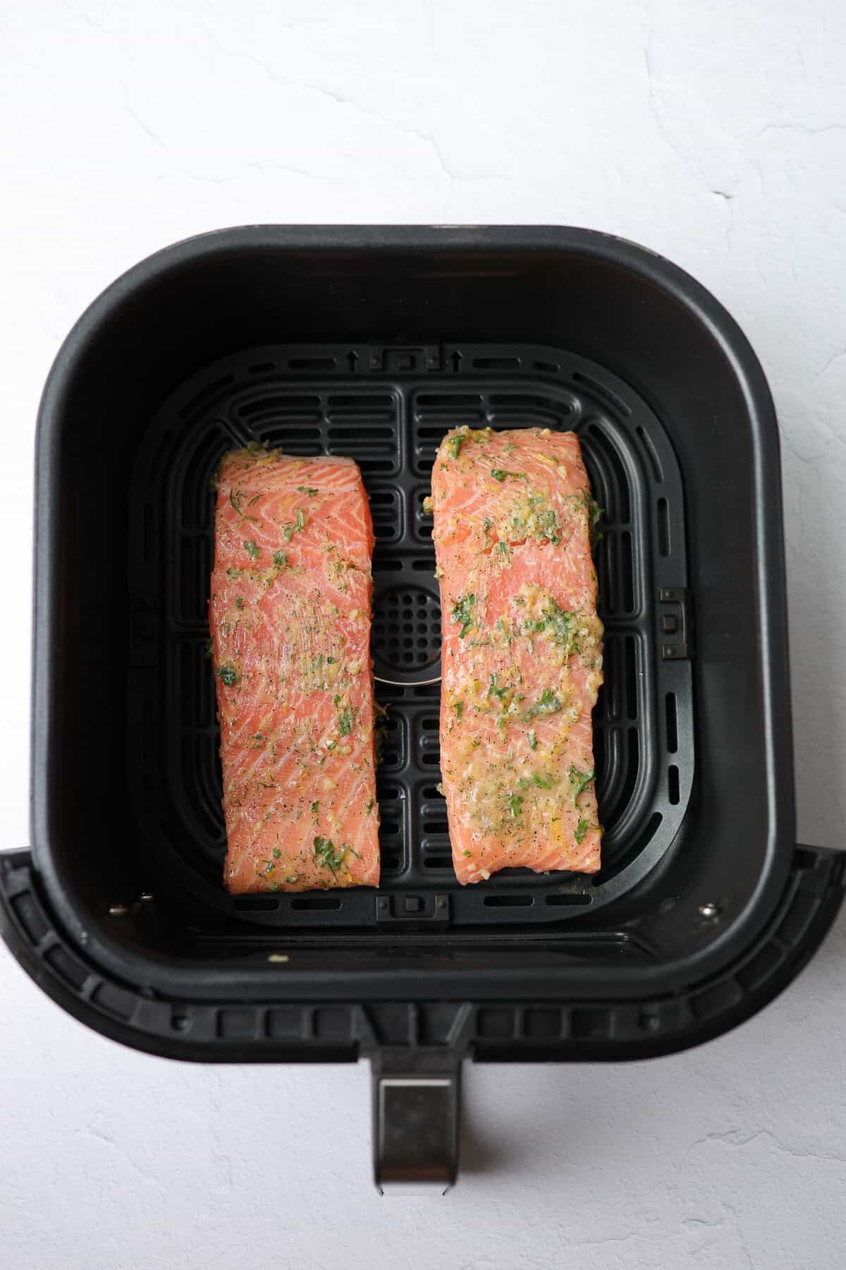 An air fryer basket with two salmon fillets covered in lemon garlic marinade.