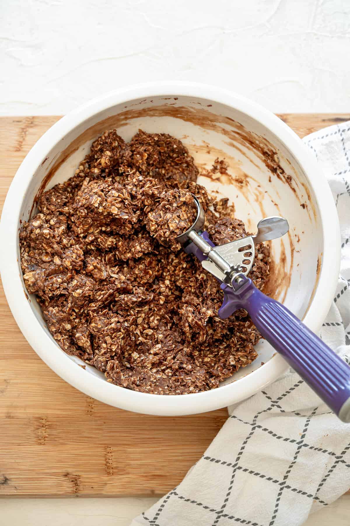 Chocolate peanut butter oatmeal mixture with a scoop in the bowl ready to be rolled into balls.