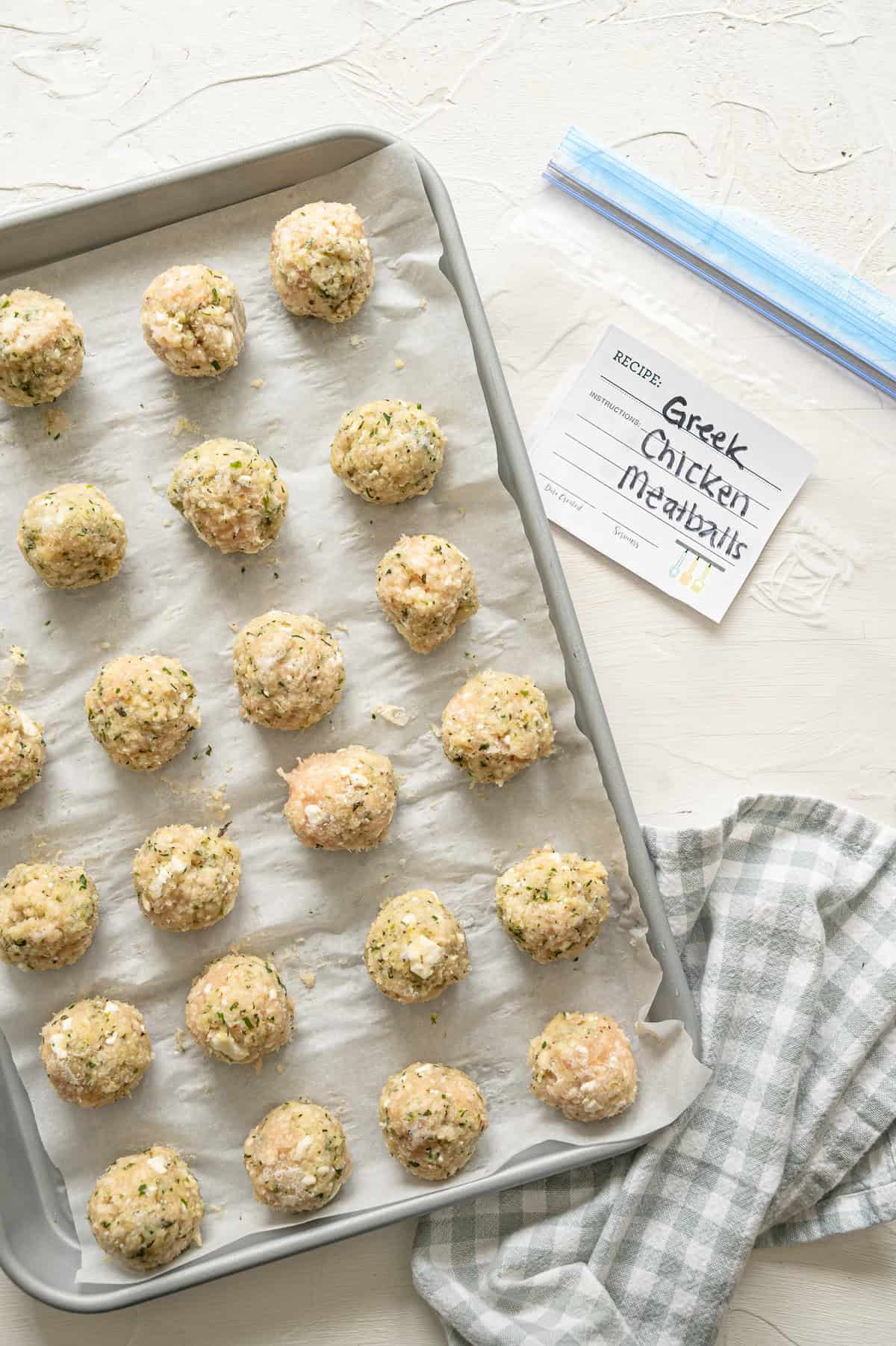 frozen Greek chicken meatballs on a sheet pan next to a labeled freezer bag.