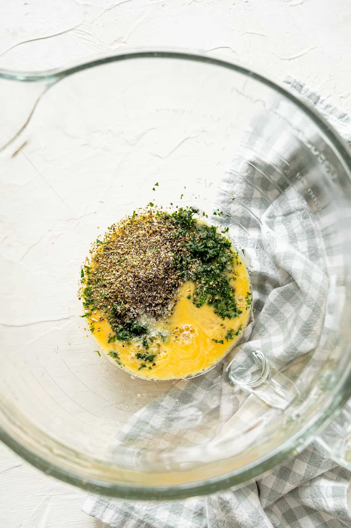 Glass bowl with eggs, seasoning, and fresh chopped herbs.