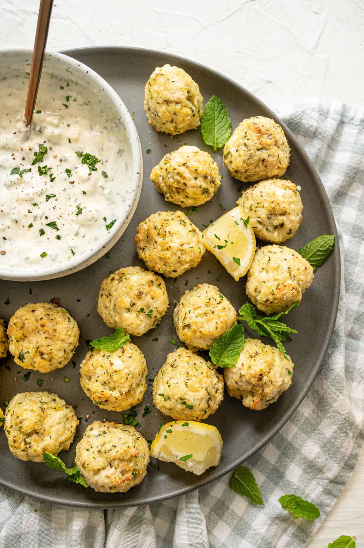 Greek chicken meatballs on a platter with a bowl of Tzatziki sauce on the side.