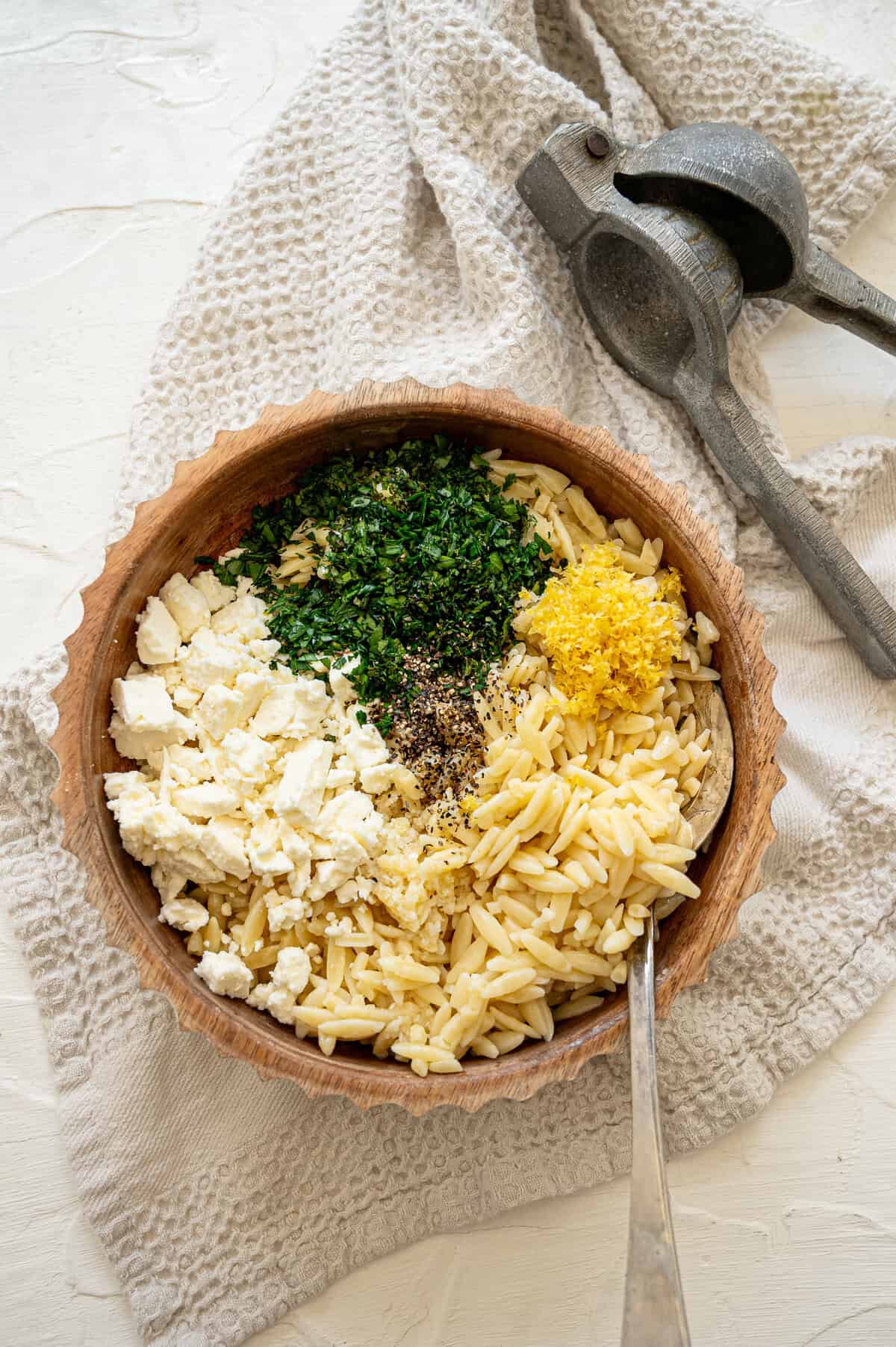 bowl with cooked orzo, feta, fresh herbs, and lemon zest all separated before stirring.