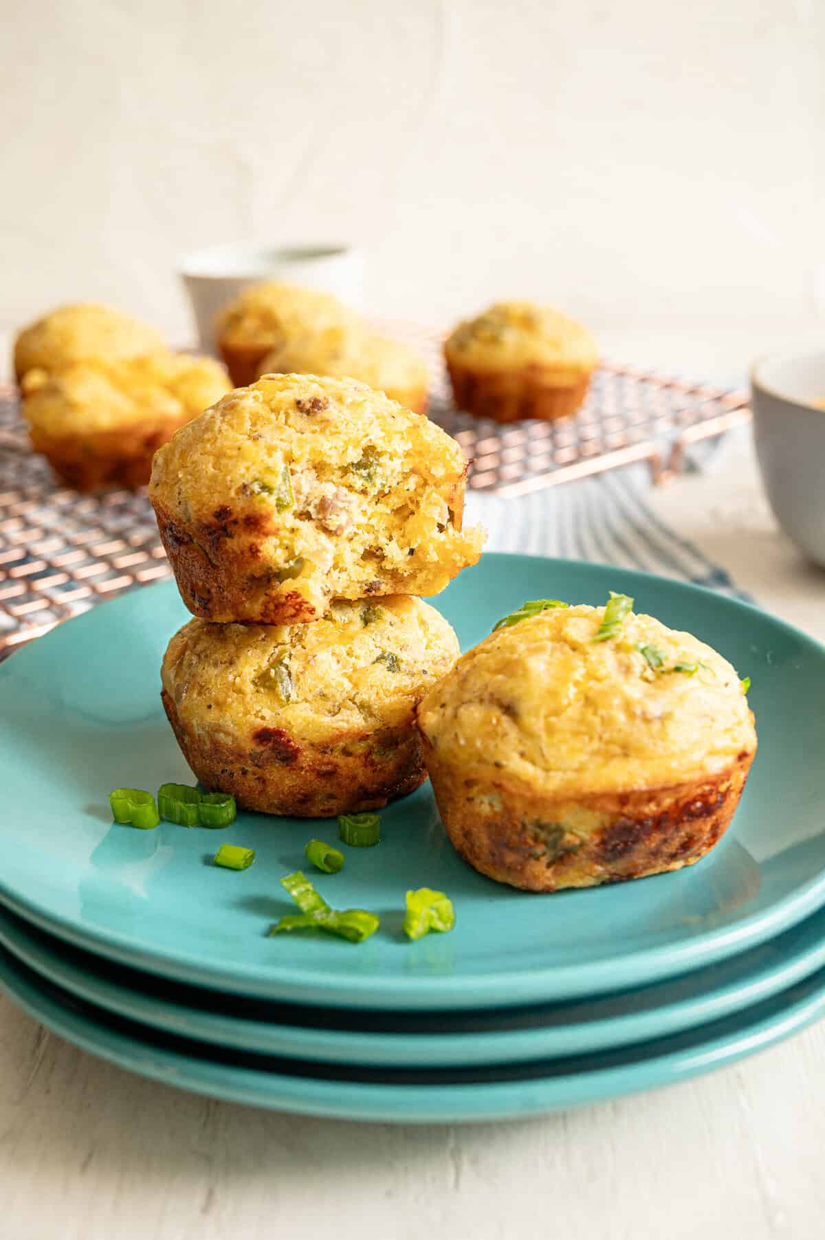 Three savory breakfast muffins stacked together on plates with chopped green onion sprinkled on them.
