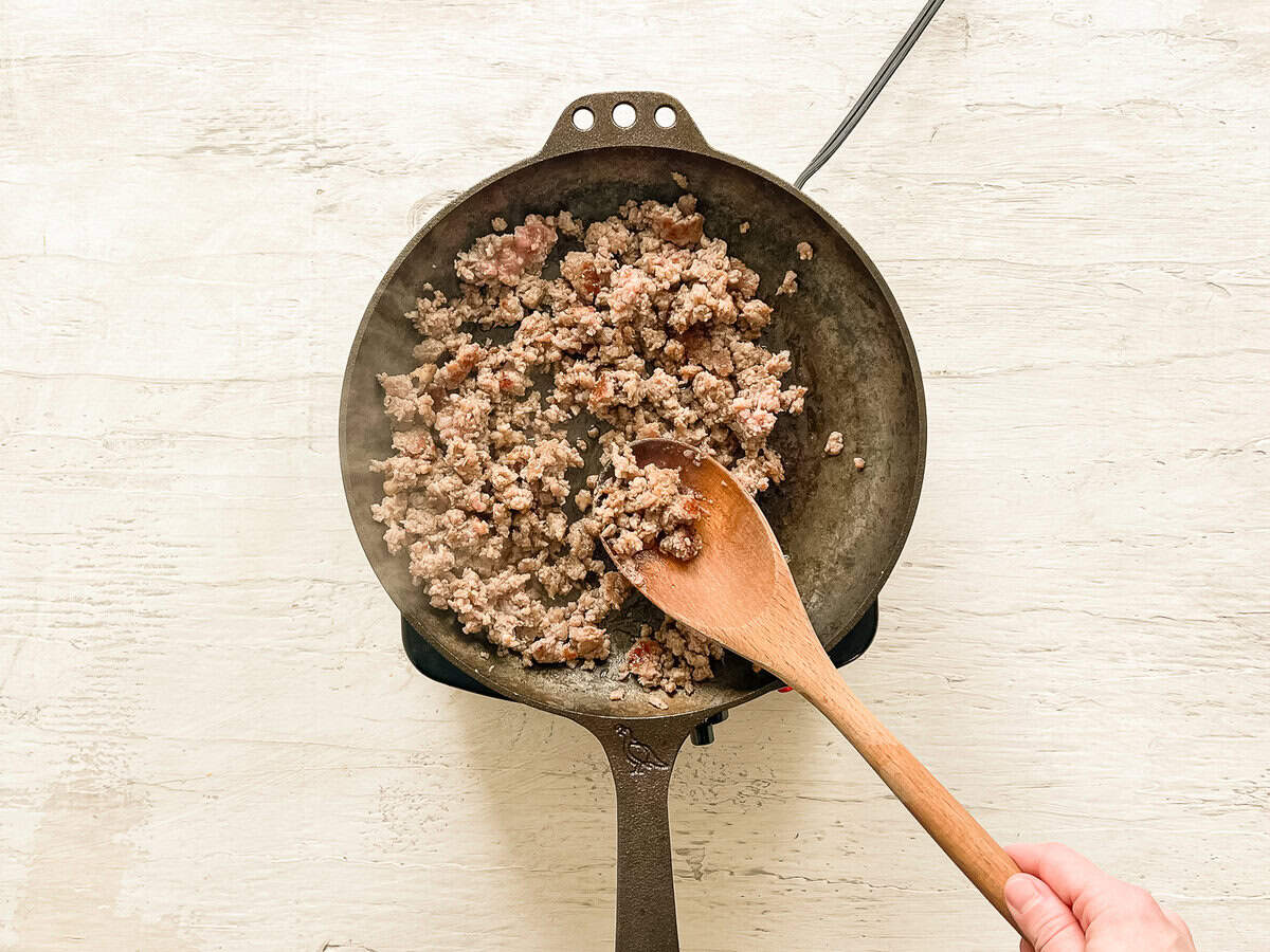 Ground breakfast sausage being browned in a cast iron skillet.