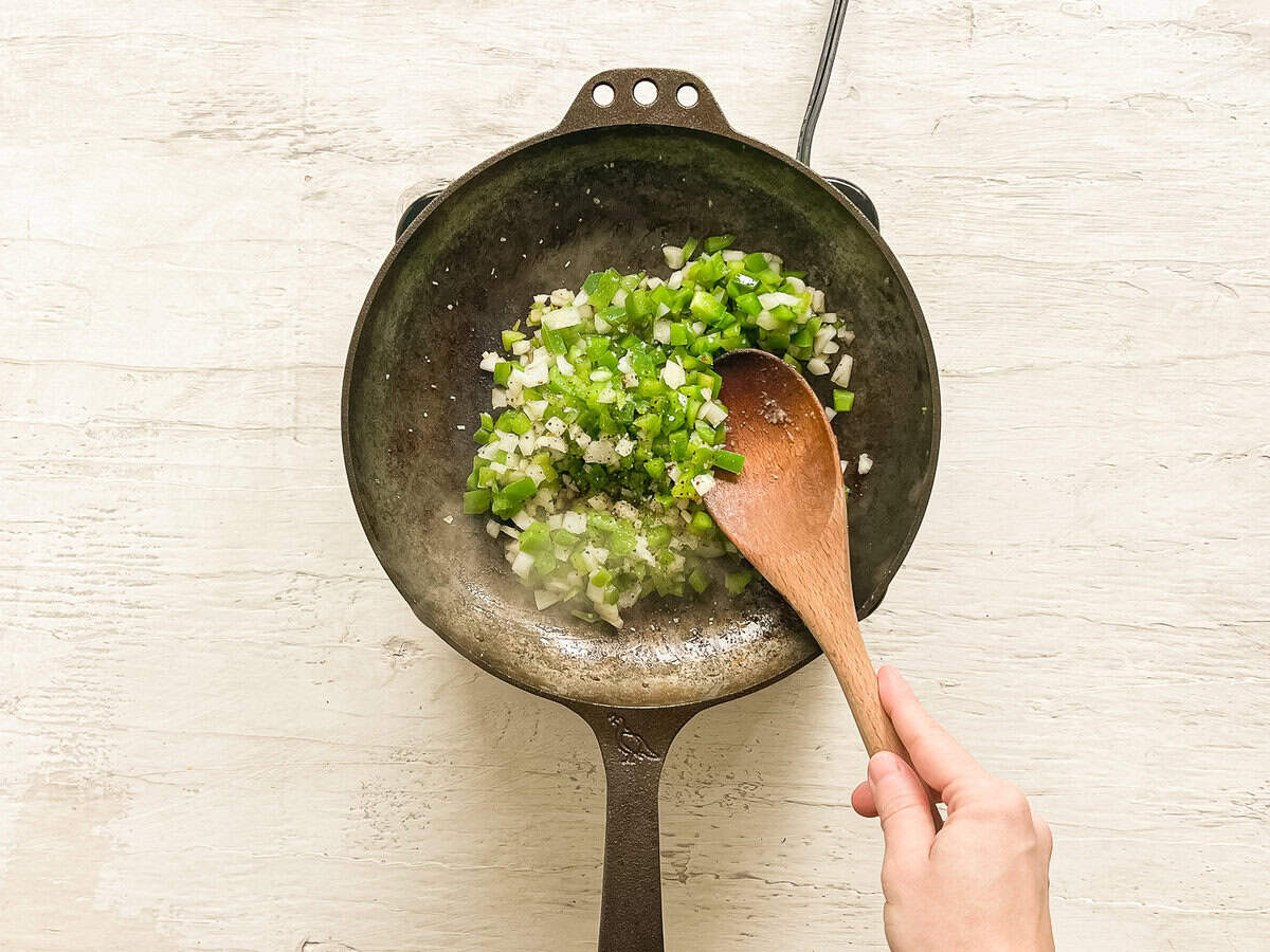 Chopped onions and green peppers sauteing in a cast iron skillet.
