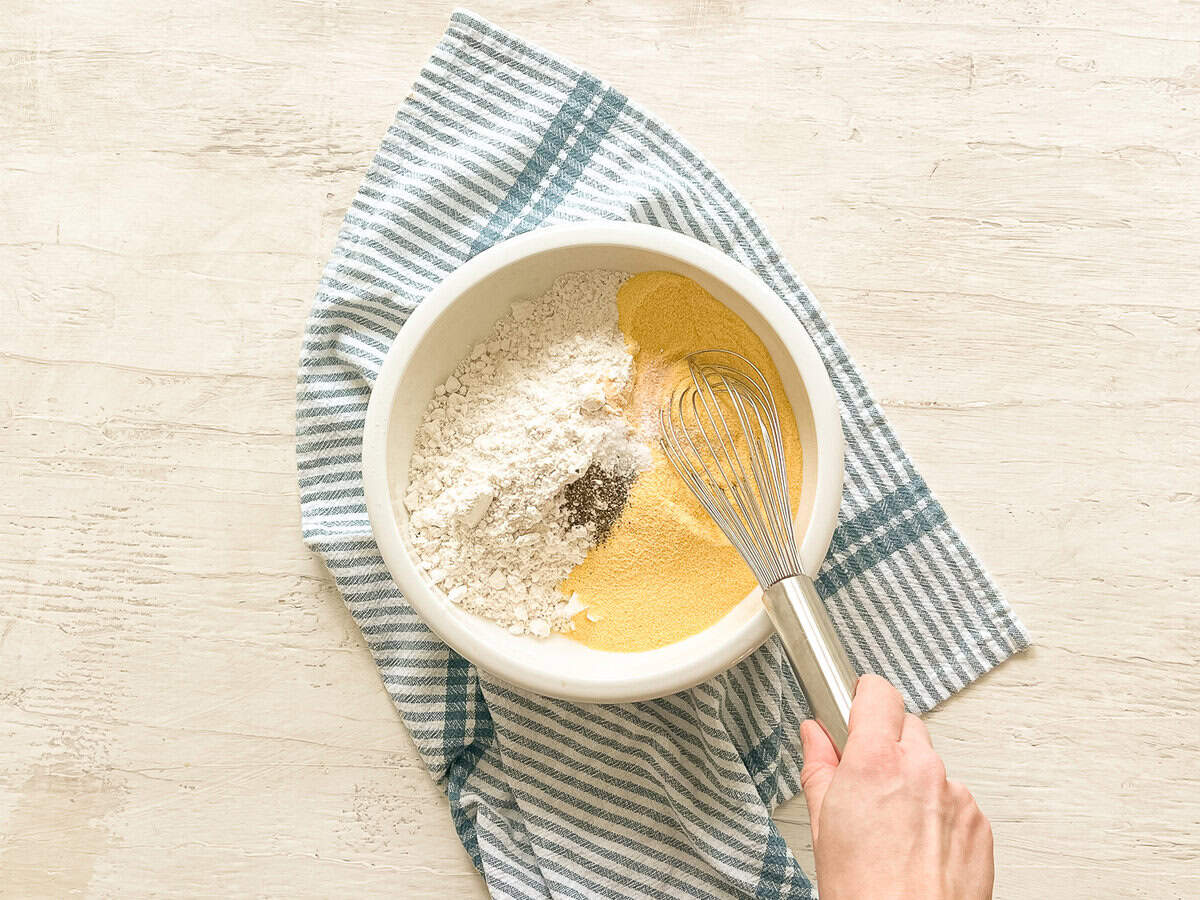 Someone whisking dry ingredients together in a white bowl.