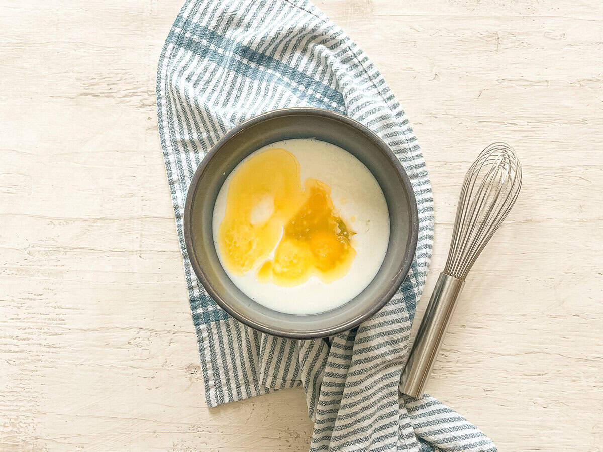 Eggs, melted butter, and buttermilk in a bowl with a whisk next to it.