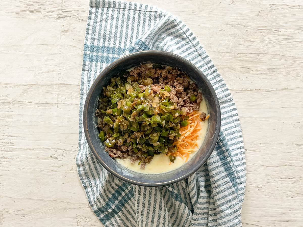 A mixing bowl with all the ingredients for savory breakfast muffins dumped in ready to be mixed together.