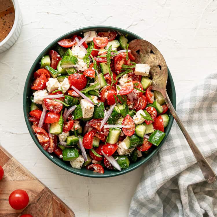Cucumber tomato feta salad with red onion toss together with a light dressing in a bowl.