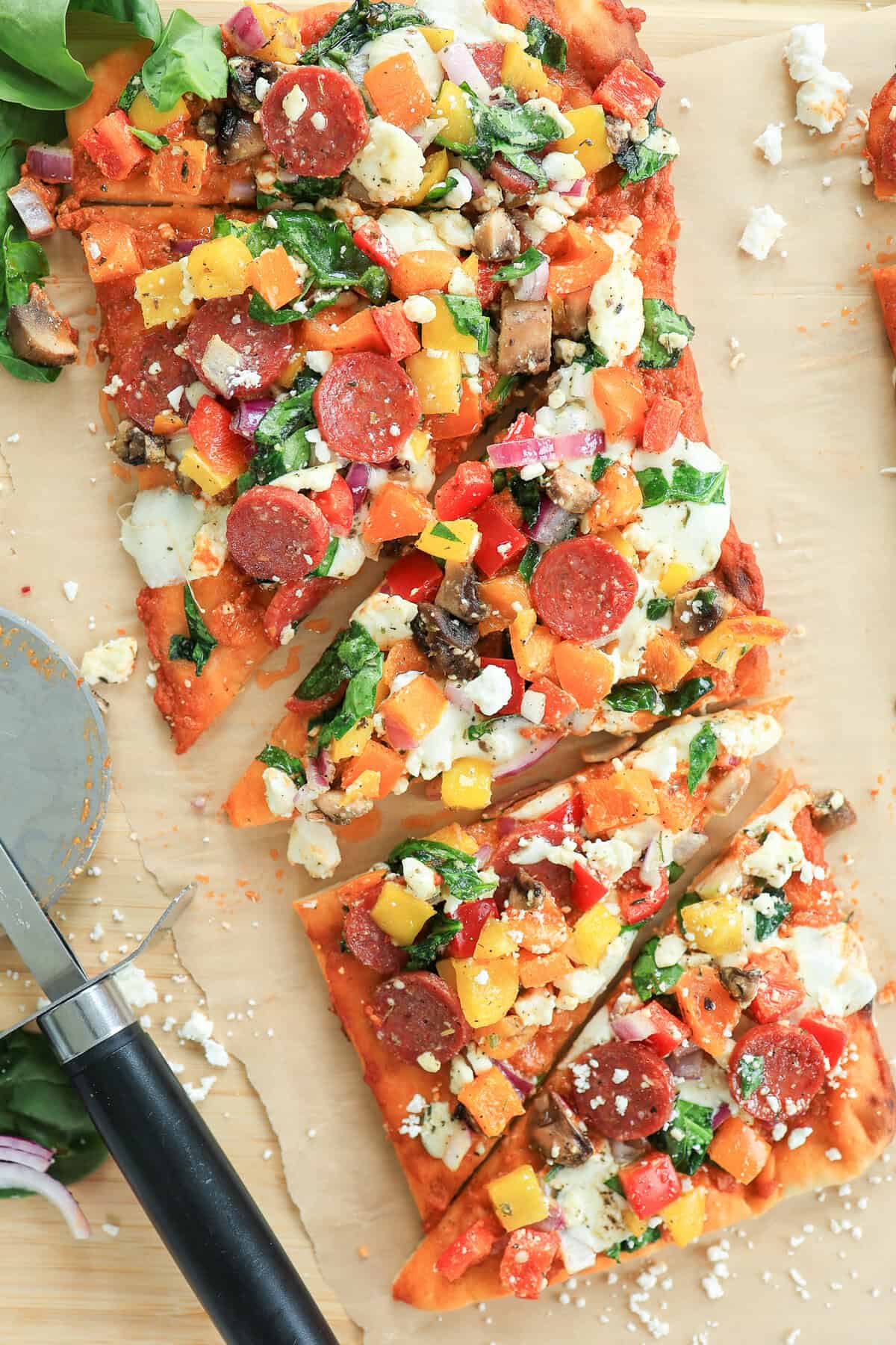 A flatbread pizza covered in veggies, pepperoni, and cheese ready to serve.