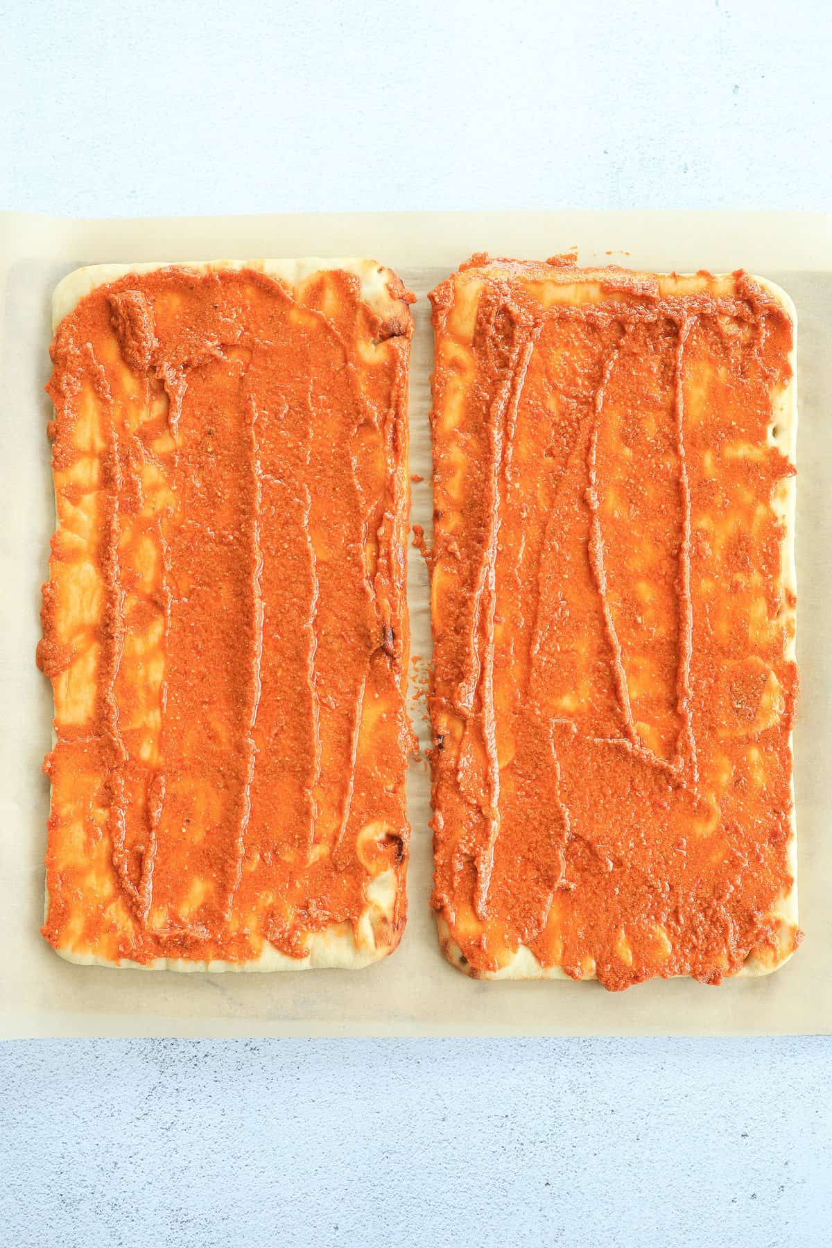 Two flatbreads covered in pizza sauce waiting for toppings.