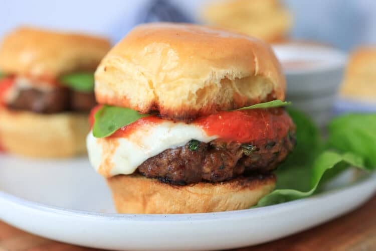 Mini Italian burger with fresh mozzarella, marinara, and basil on top.