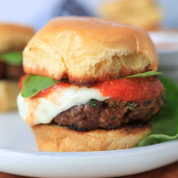 Mini Italian burger with fresh mozzarella, marinara, and basil on top.