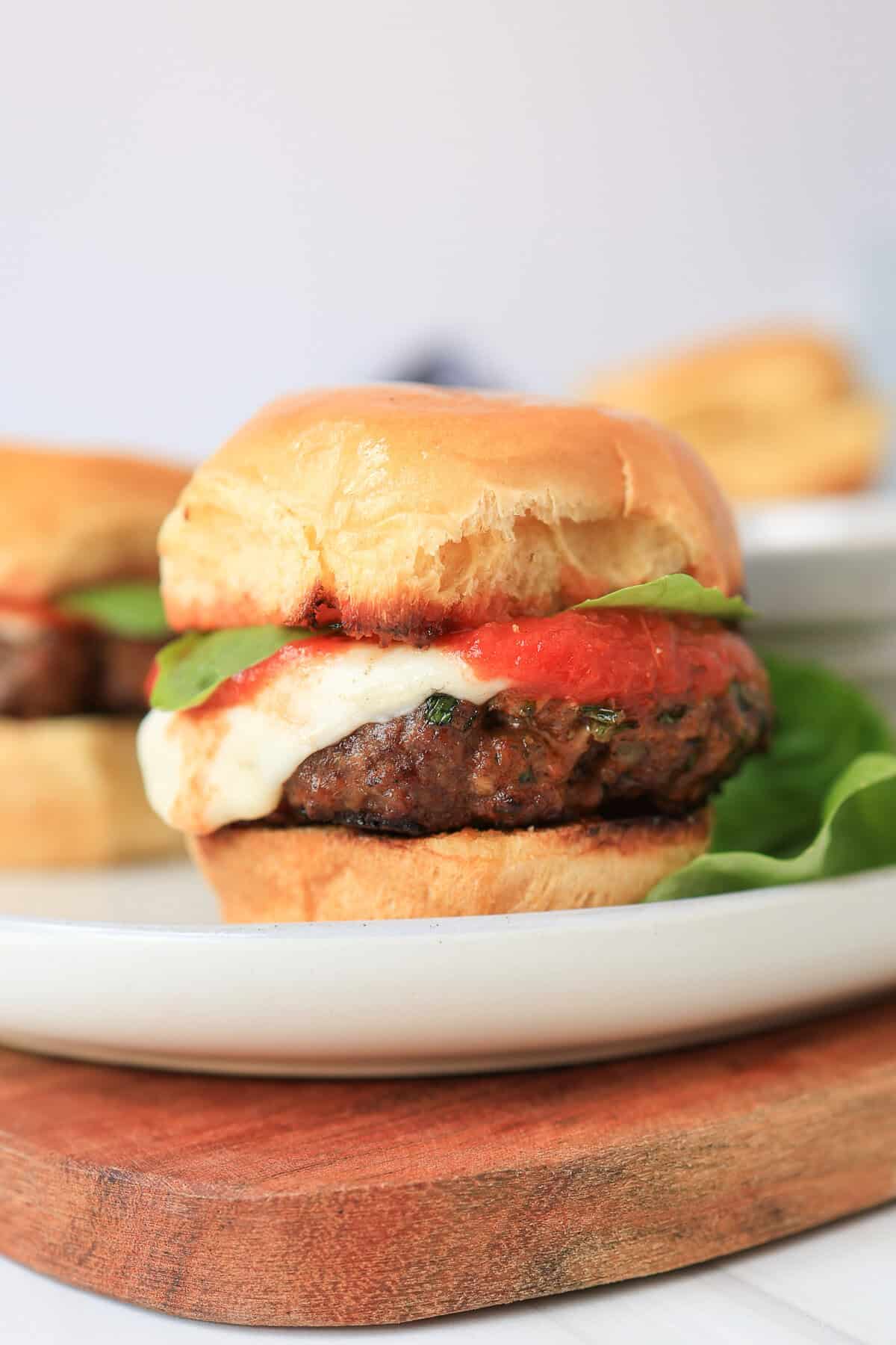 Mini Italian burger with fresh mozzarella, marinara, and basil on top.