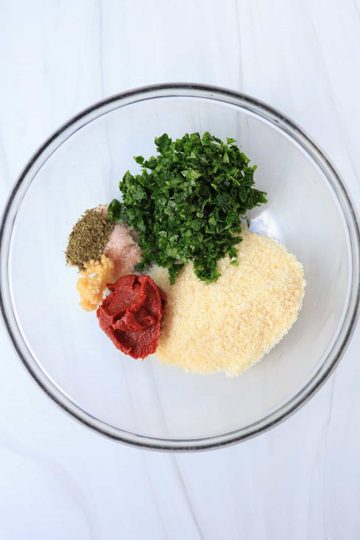 Seasonings, fresh minced parsley, Parmesan cheese, and tomato paste in a mixing bowl.
