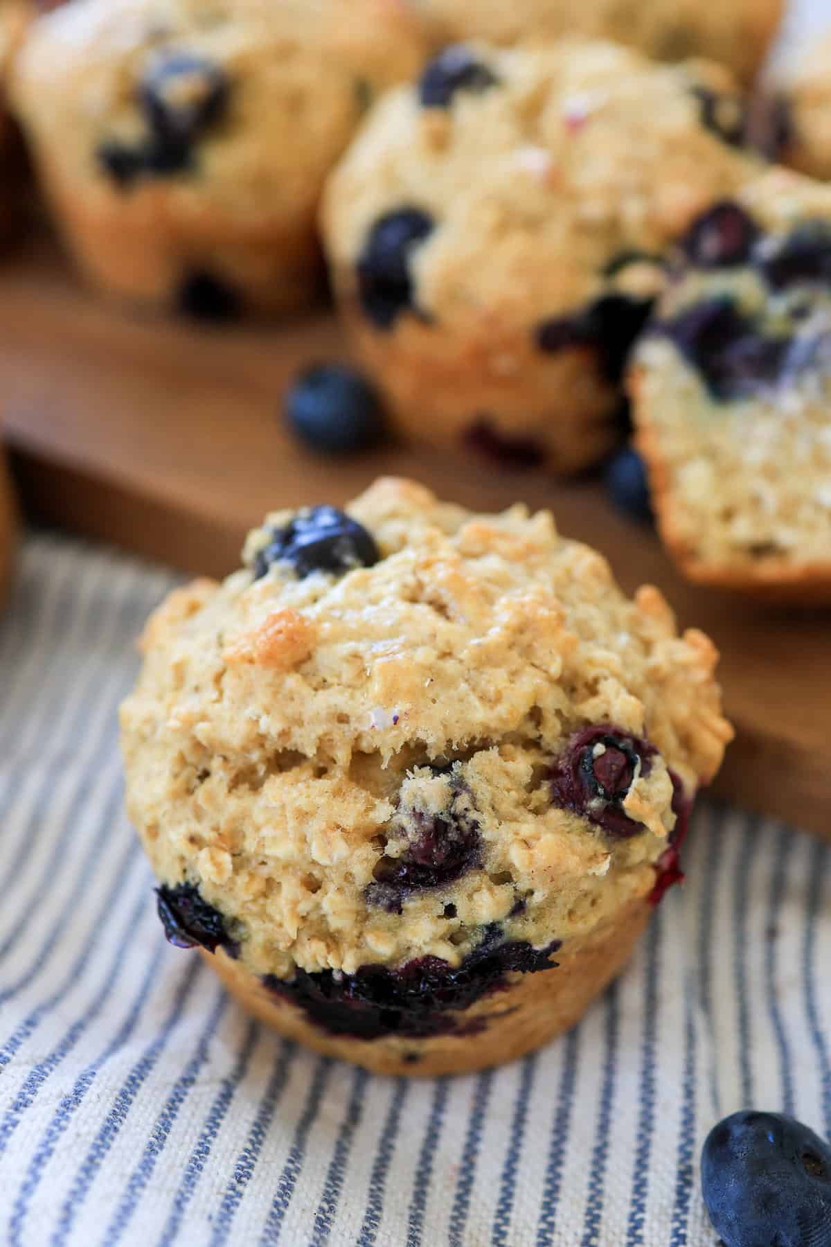 Blueberry muffin on a thin blue striped tea towel with more muffins in the background.