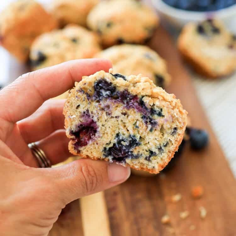 A hand holding a blueberry oatmeal muffin half so you can see the inside texture.
