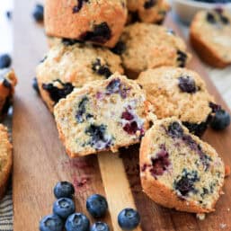 Blueberry oatmeal muffins cut in half and stacked on a cutting board.
