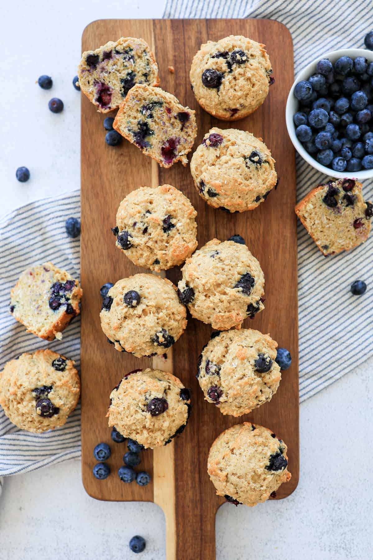 Blueberry oatmeal muffins and a bowl of blueberries on a wooden cutting board to serve.