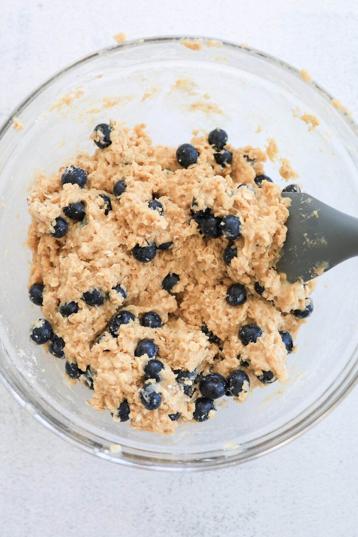 A spoon folding blueberries into thick muffin batter.
