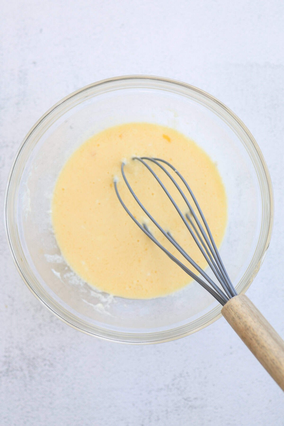 Wet ingredients for muffins being whisked together in a glass bowl.