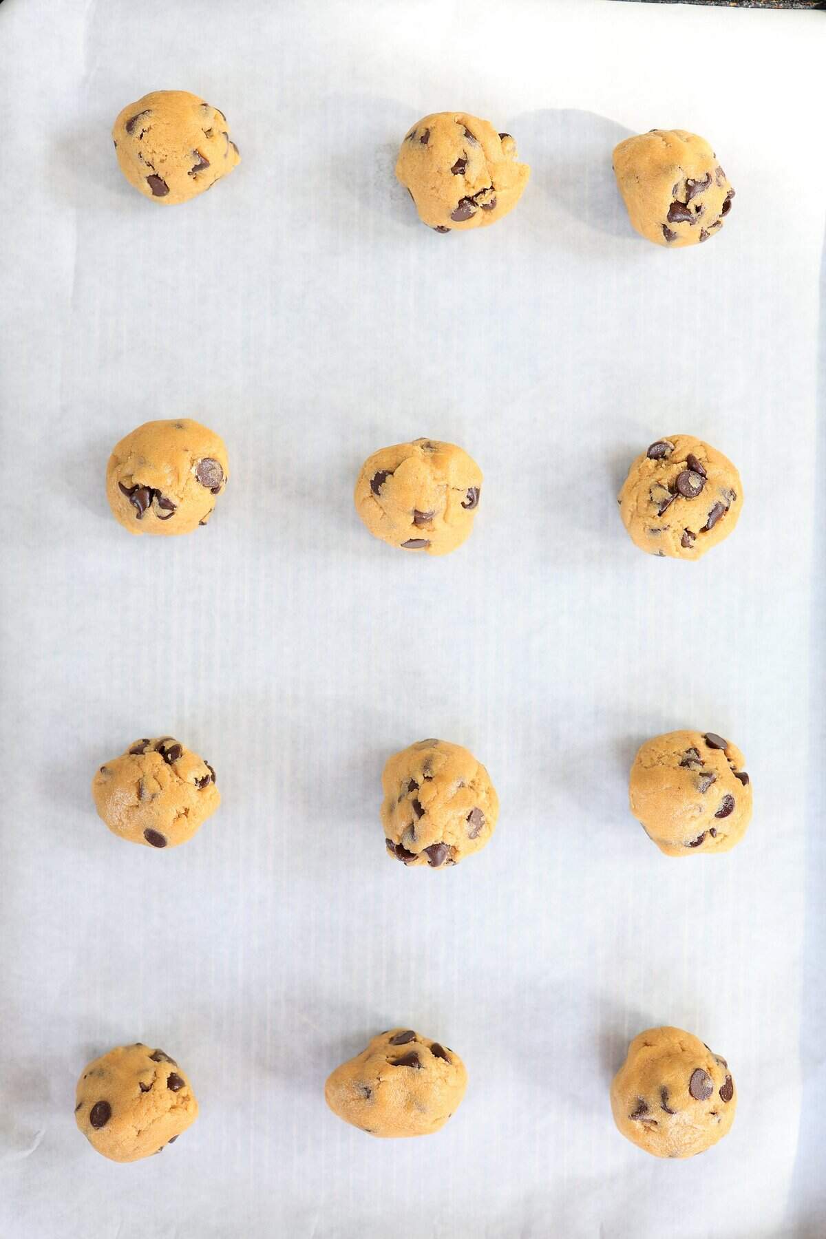 Balls of chocolate chip cookie dough on a parchment-lined baking sheet.