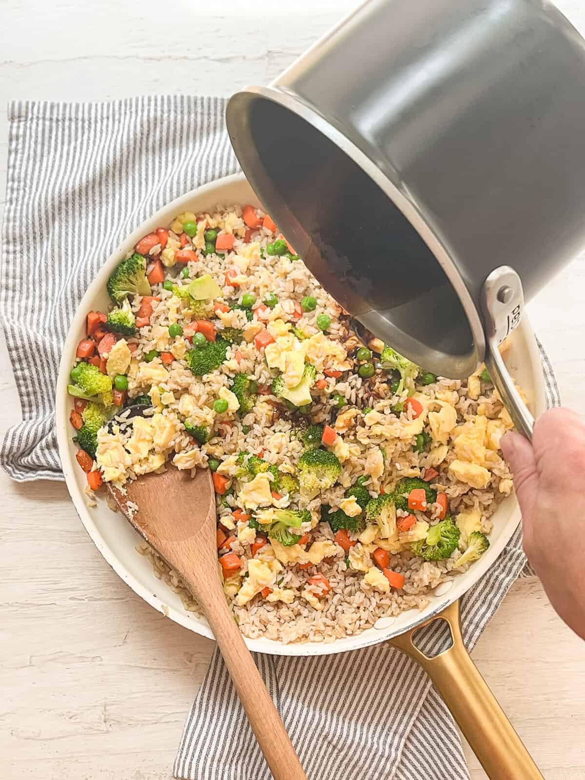 Sweet soy sauce being poured in to a skillet of egg fried rice.