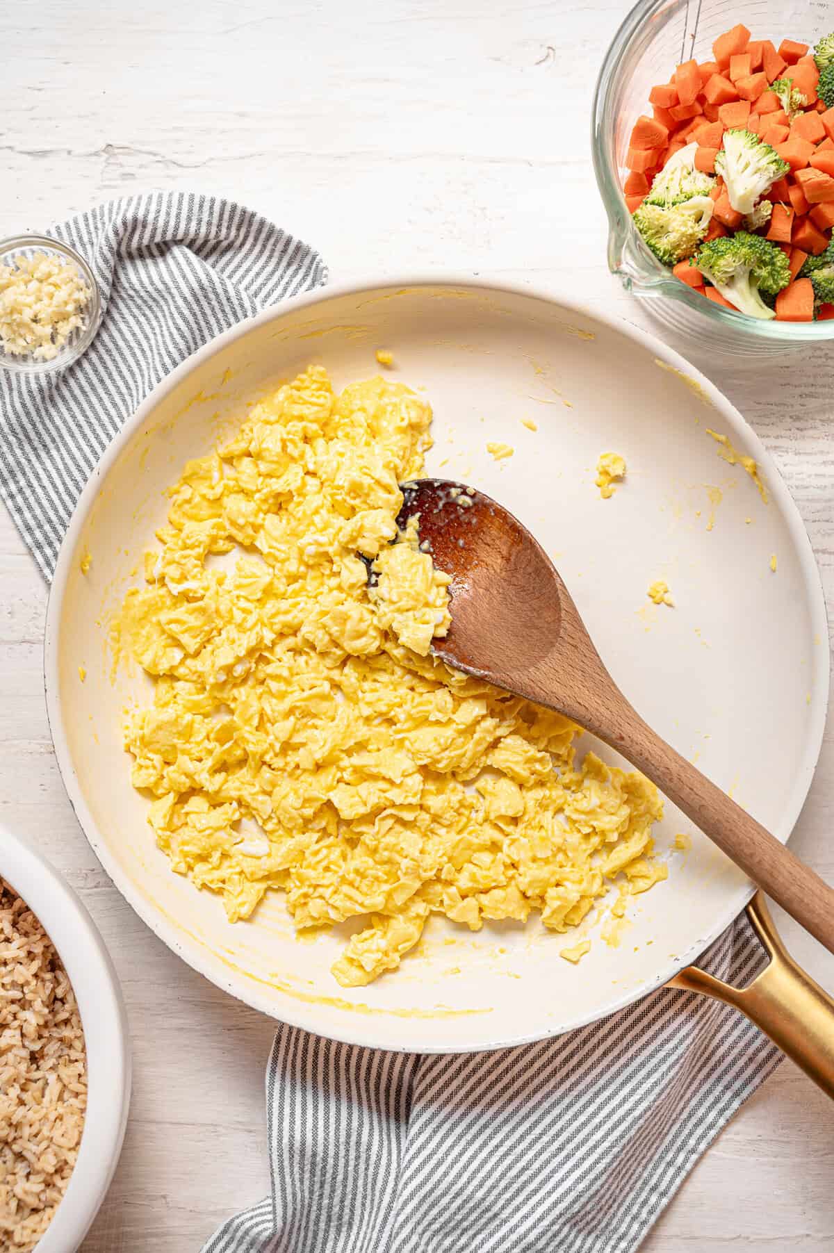 Scrambled eggs in a frying pan with a wooden spoon.