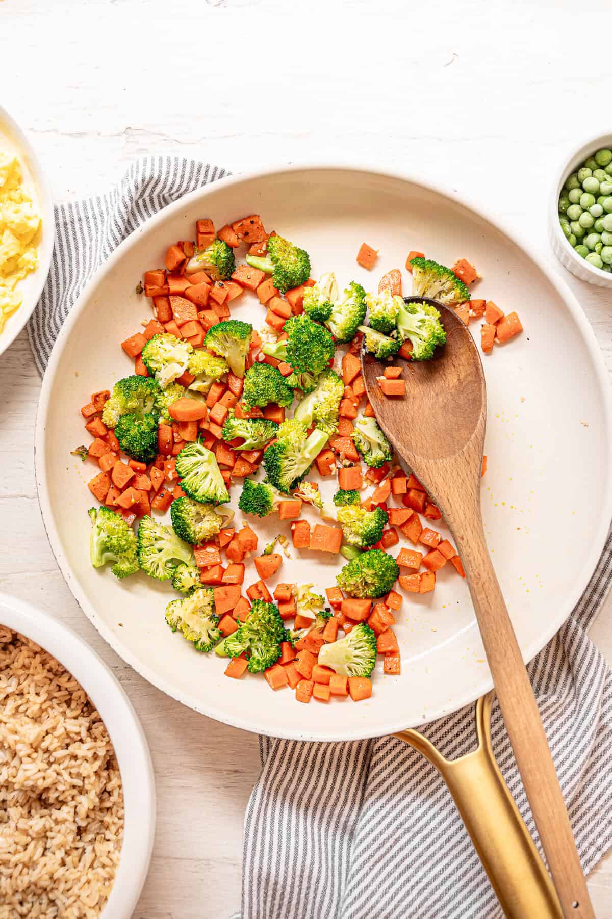 Chopped carrots and broccoli being sauteed in a skillet.