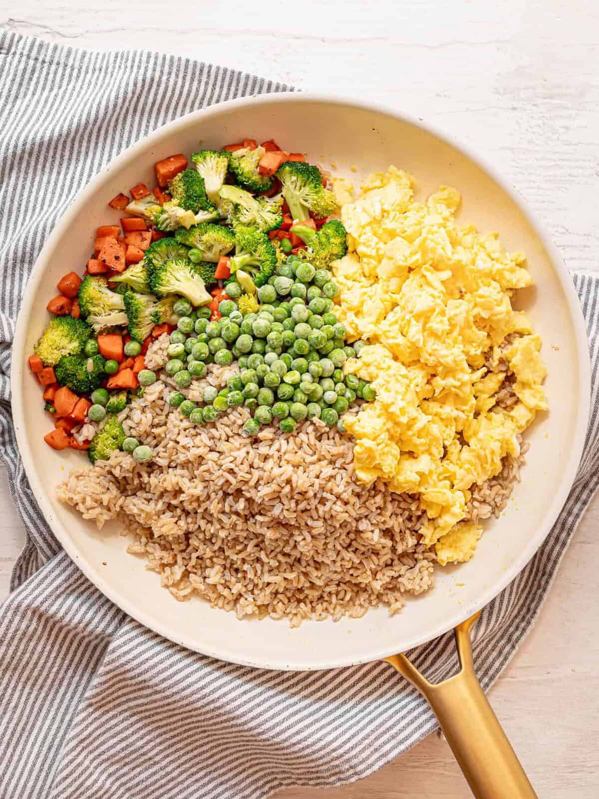 Ingredients for egg fried rice piled separately in a frying pan.