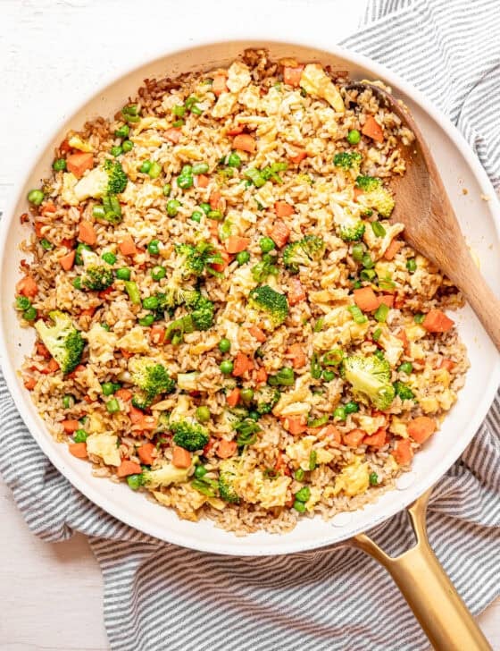 Egg fried rice being stirred in a skillet with a wooden spoon.