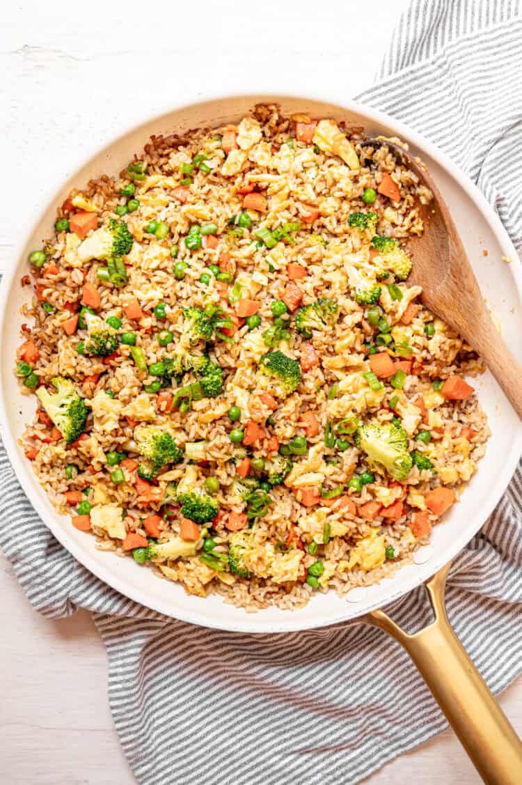 Egg fried rice being stirred in a skillet with a wooden spoon.