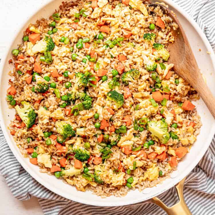 Egg fried rice being stirred in a skillet with a wooden spoon.